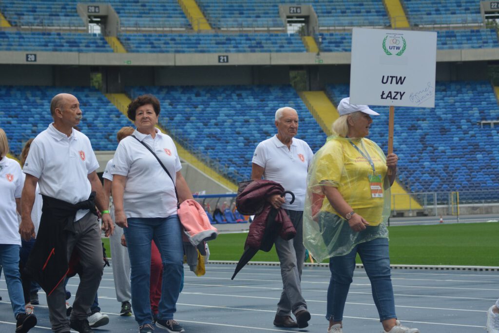 seniorzy na stadionie niosą tablicę UTW w Łazach