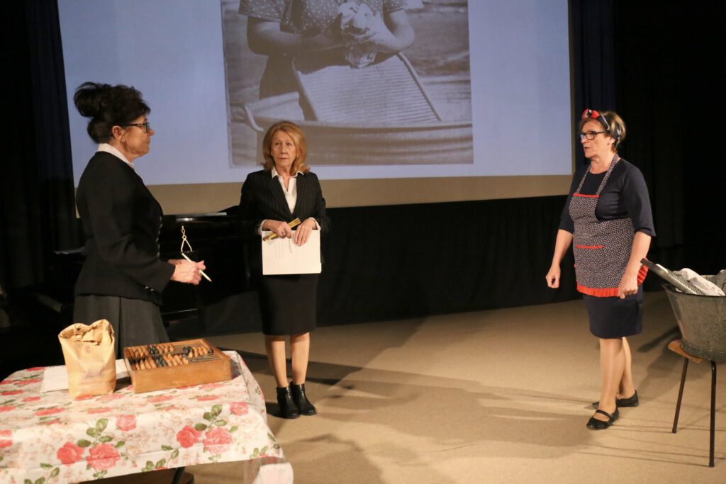 grupa teatralna UTW, trzy kobiety na scenie na tle  wyświetlonej prezentacji