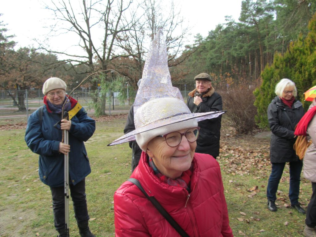 seniorzy  stoją w plenerze, jedna kobieta ma kapelusz czarownicy na głowie