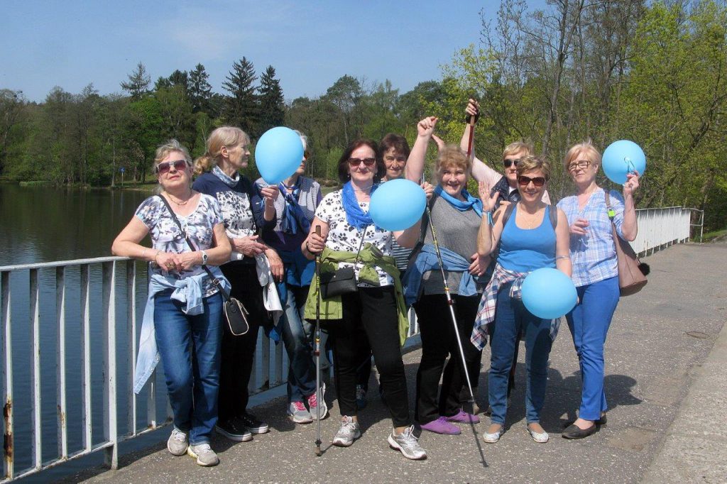 zdjęcie grupowe seniorów z niebieskimi balonami i kijkami przy jeziorze