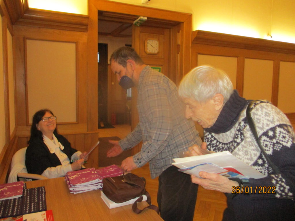 Spotkanie autorskie Marii Nawrot, seniorzy przeglądają tomiki z wierszami i ulotki