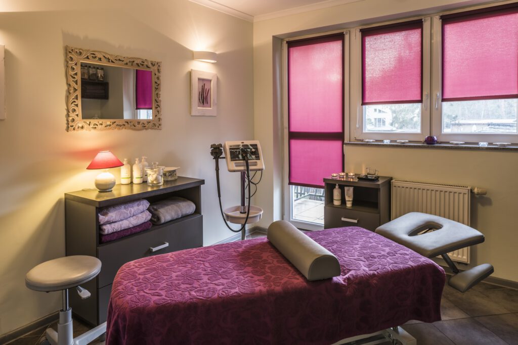 pokój masażu z dwiema szafkami, różowymi ręcznikami dla gości, leżanka, krzesło i wyjście na balkon 